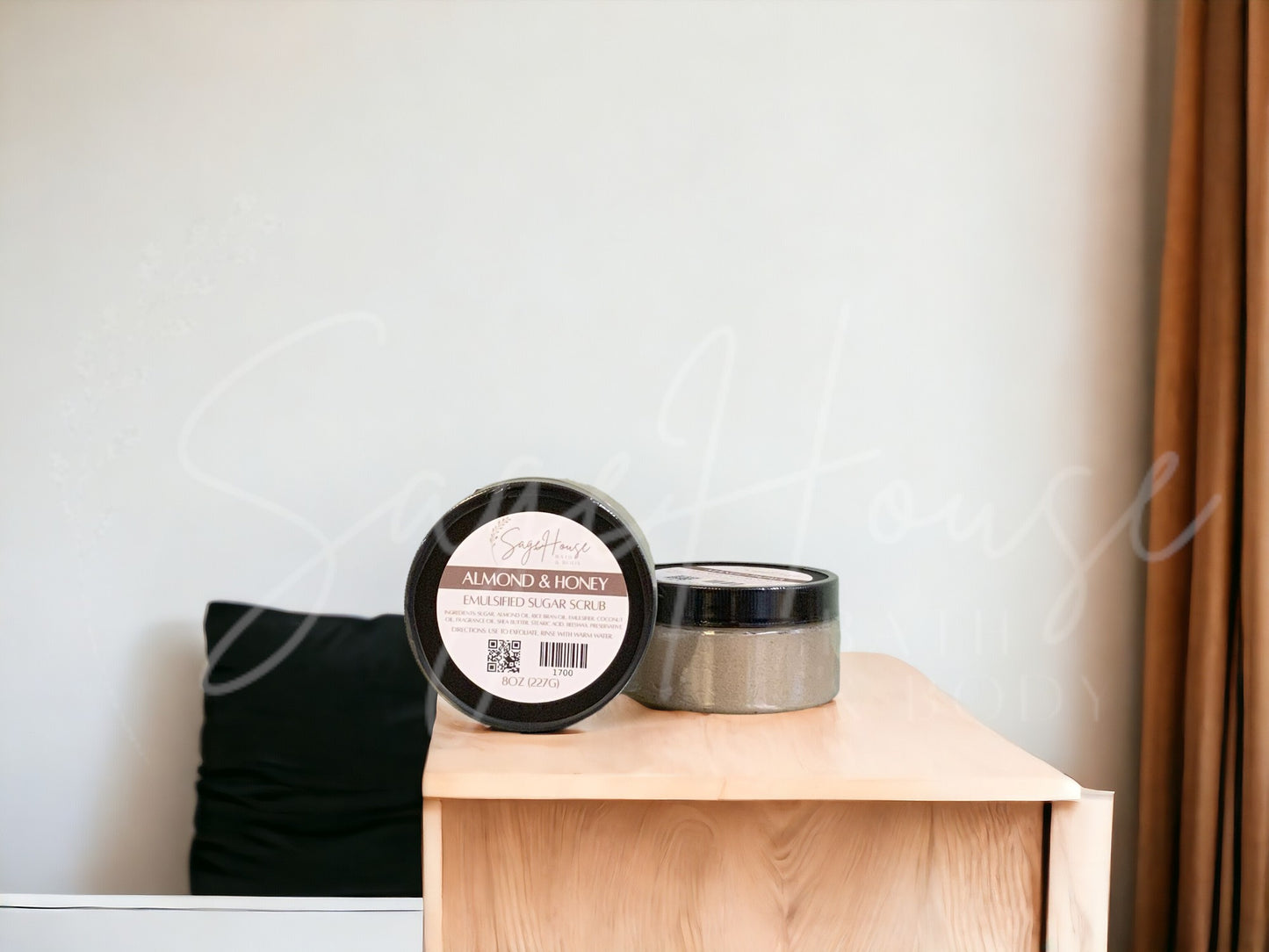 A jar of Almond And Honey Sugar Scrub is placed on a wooden surface.