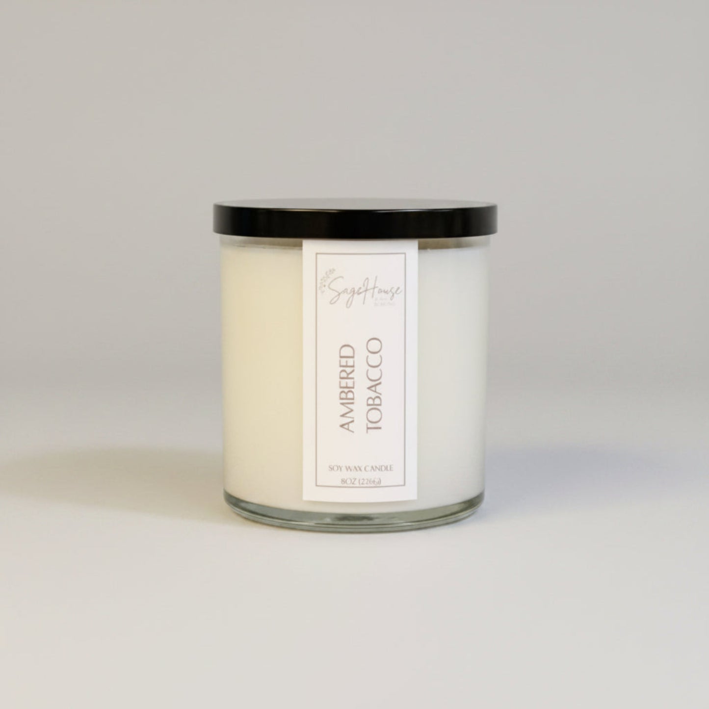 A white soy wax candle in a clear container, placed on a wooden surface, with a label on the front.