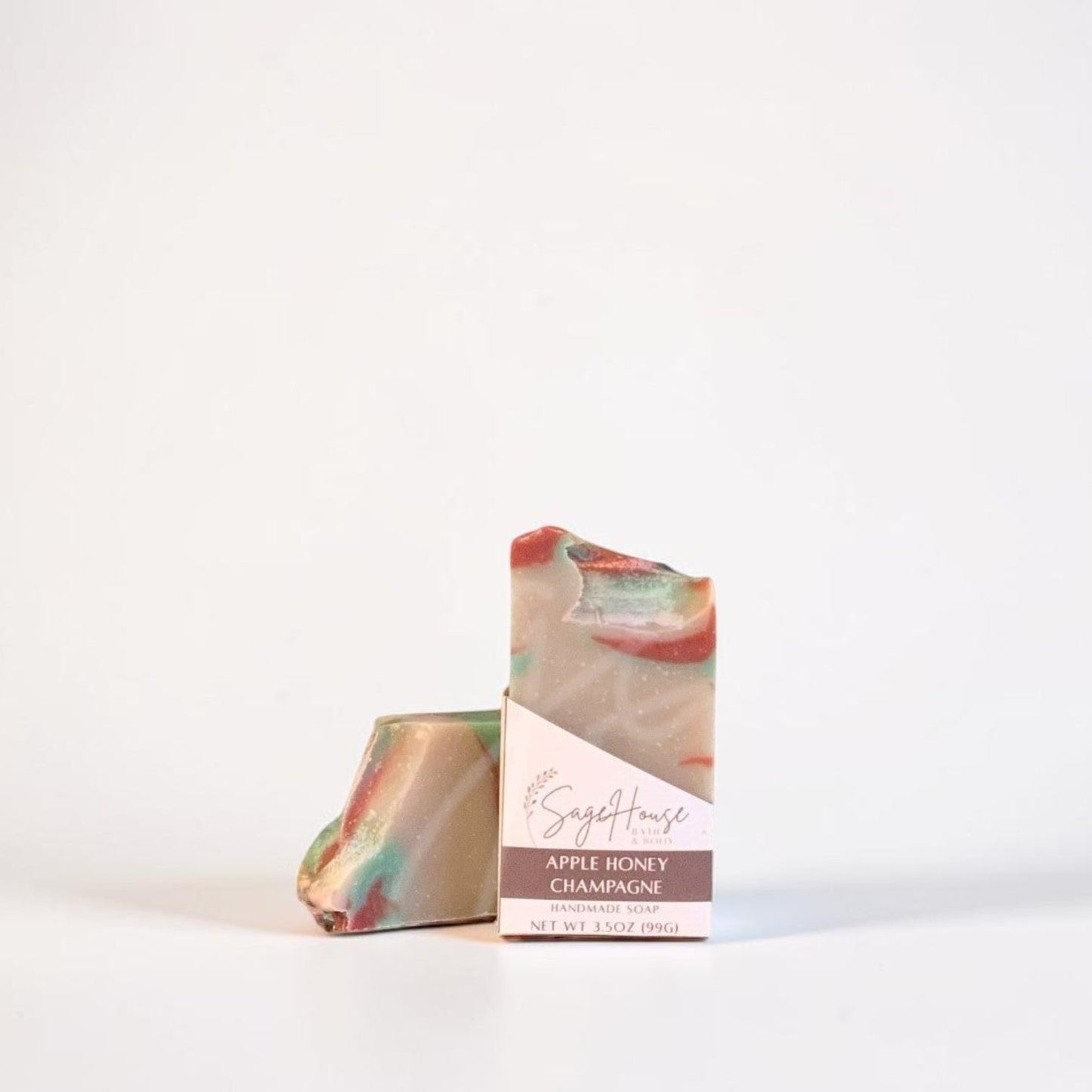 A handmade soap bar with a marbled pattern of pink, green, and beige, standing next to its paper packaging sleeve on a clean white background.
