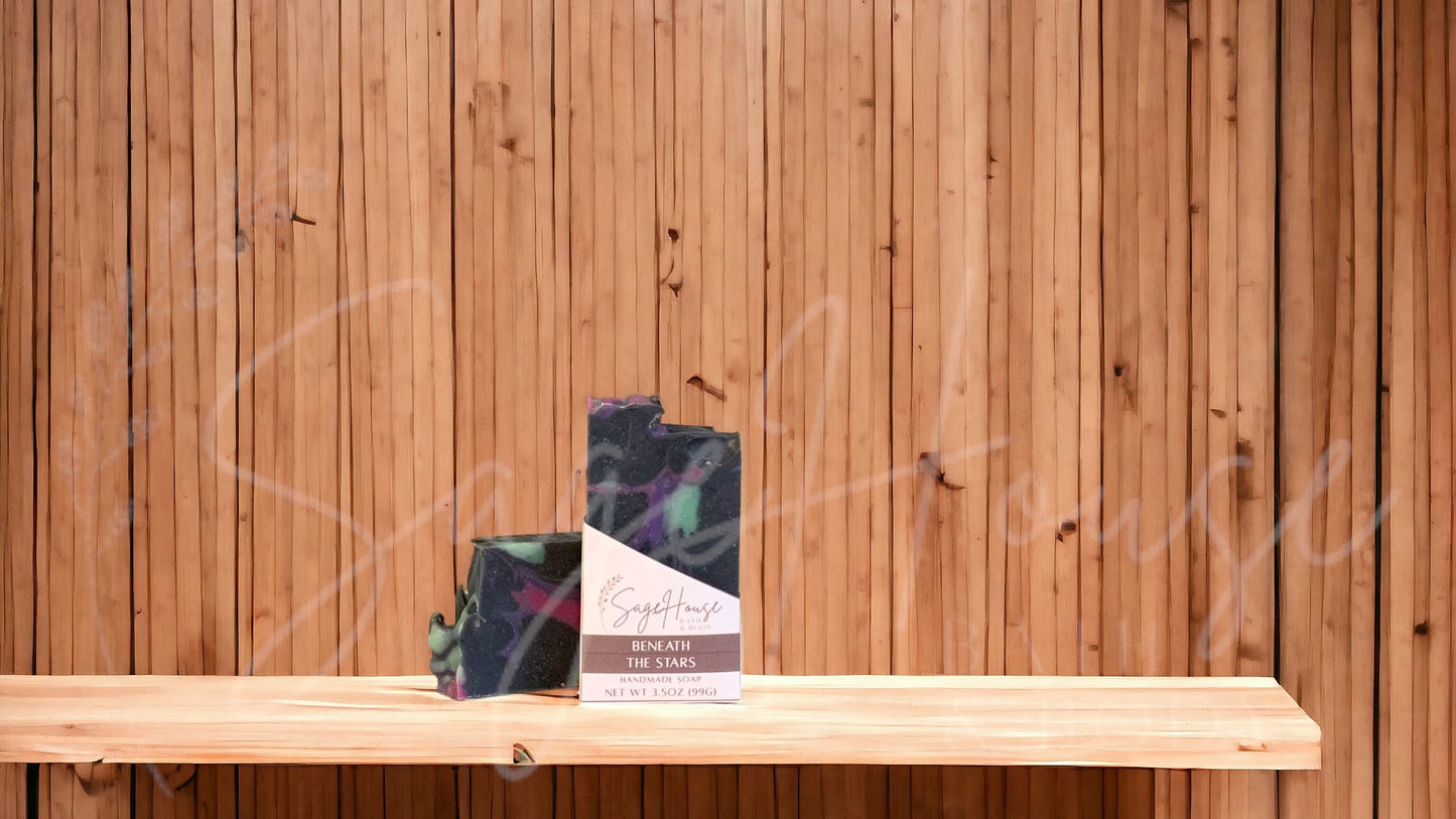 A black bar of soap with green, purple and pink accents in a white labeled box, on a wood surface.