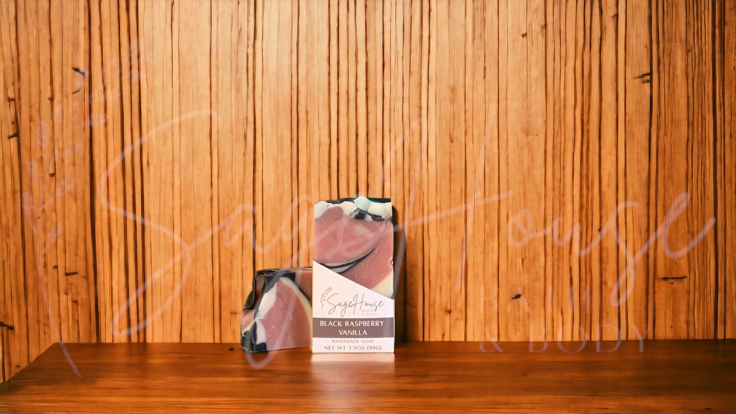 A mauve colored bar of soap with accents of white and black in a white labeled box, on a wood surface.
