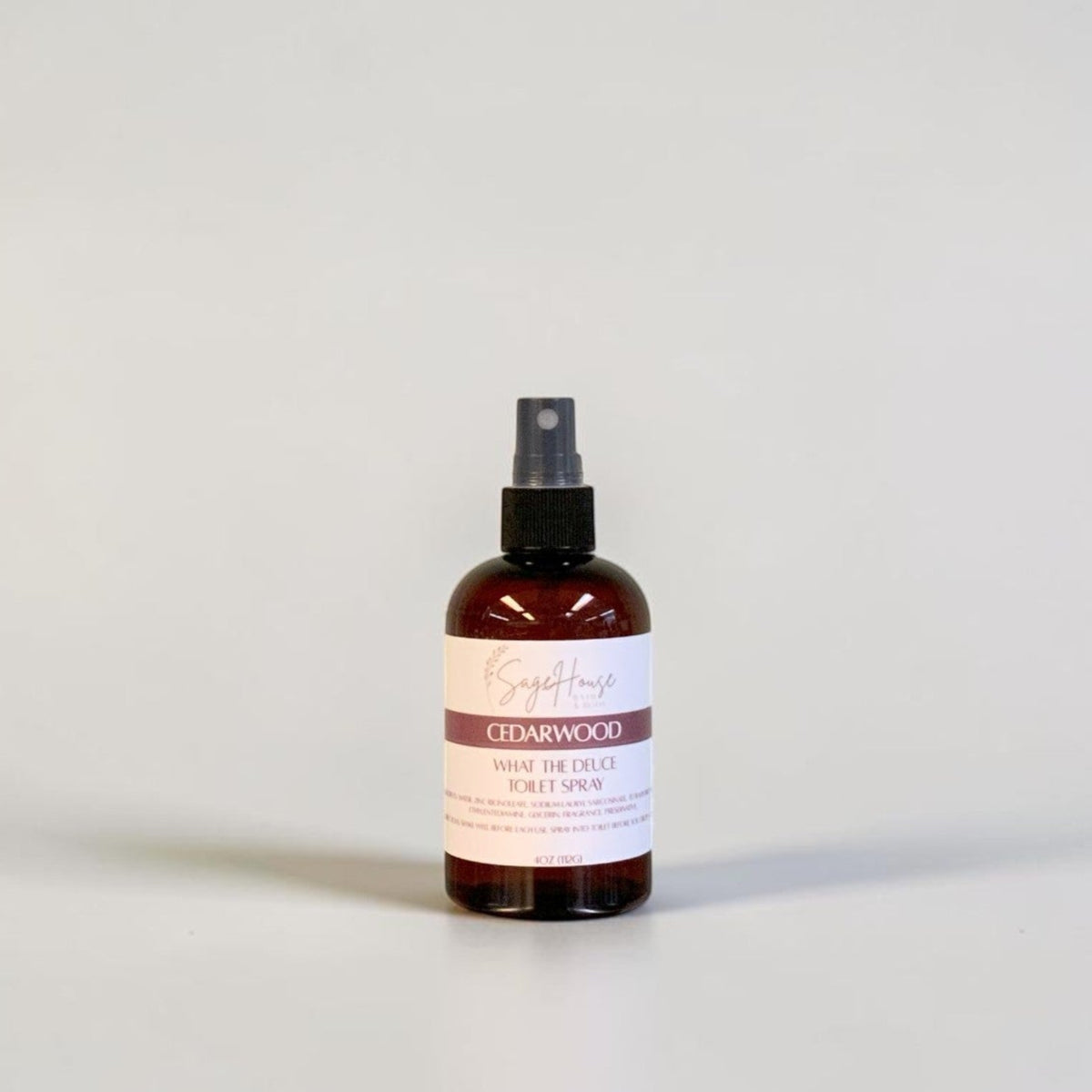 An amber spray bottle with black spray nozzle and white label, standing on a light gray surface against a light gray background.