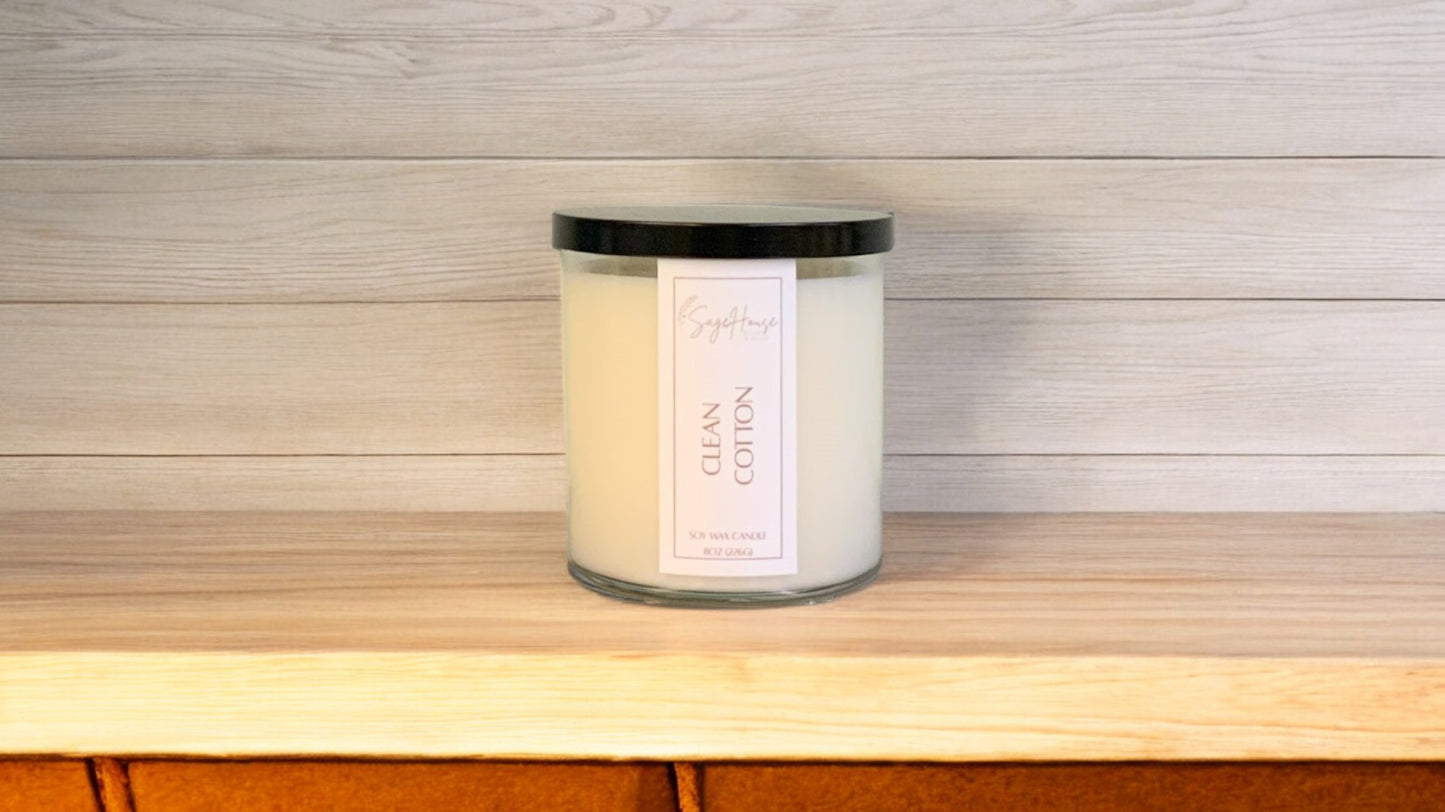 A white soy wax candle in a clear container, placed on a wooden surface, with a label on the front.