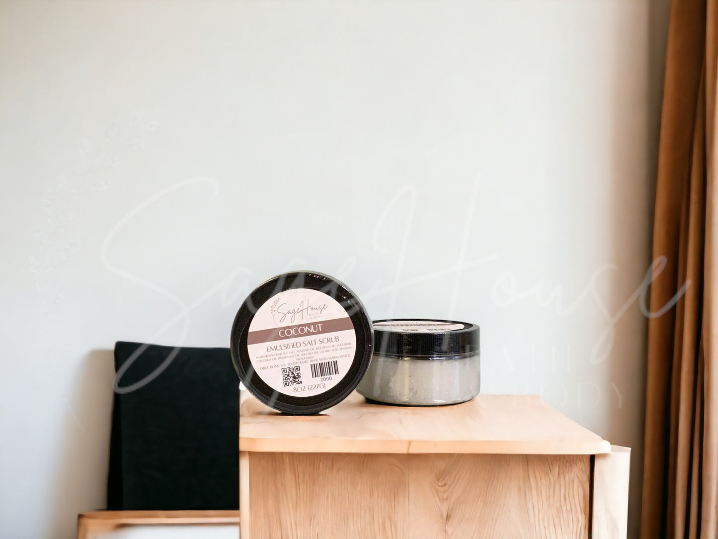 Two jars of scrub, one standing next to the other, sitting on a wooden surface with a white background