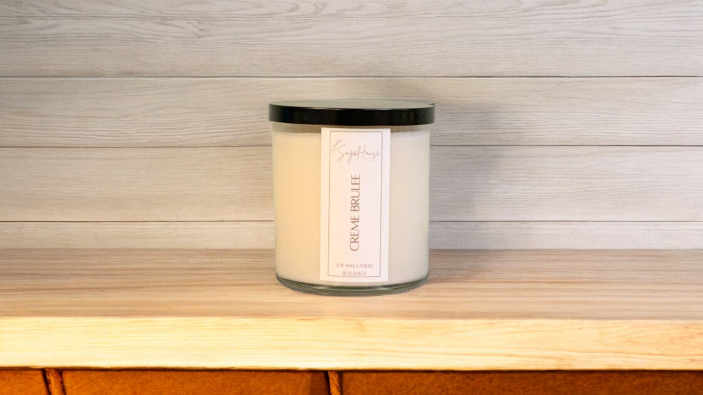 A white soy wax candle in a clear container, placed on a wooden surface, with a label on the front.