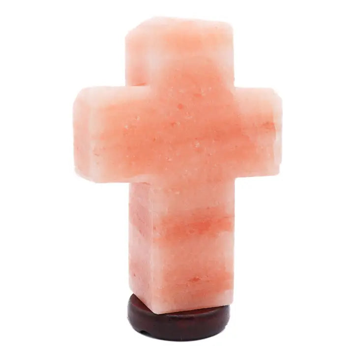 Cross-shaped pink Himalayan salt lamp on a brown base, illuminated