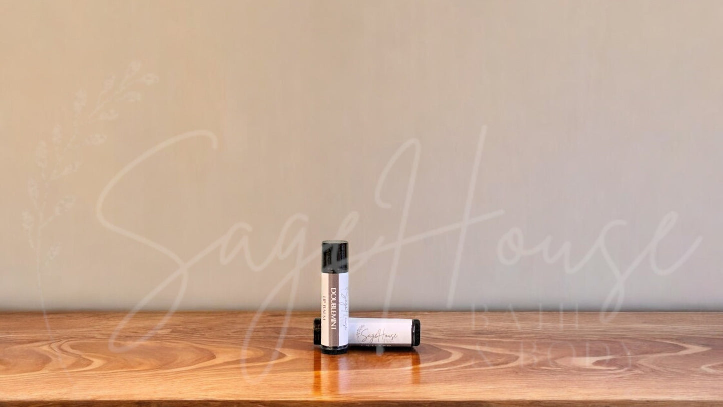 A tube of doublemint lip balm placed upright with a tube lying behind it, on a wooden surface.