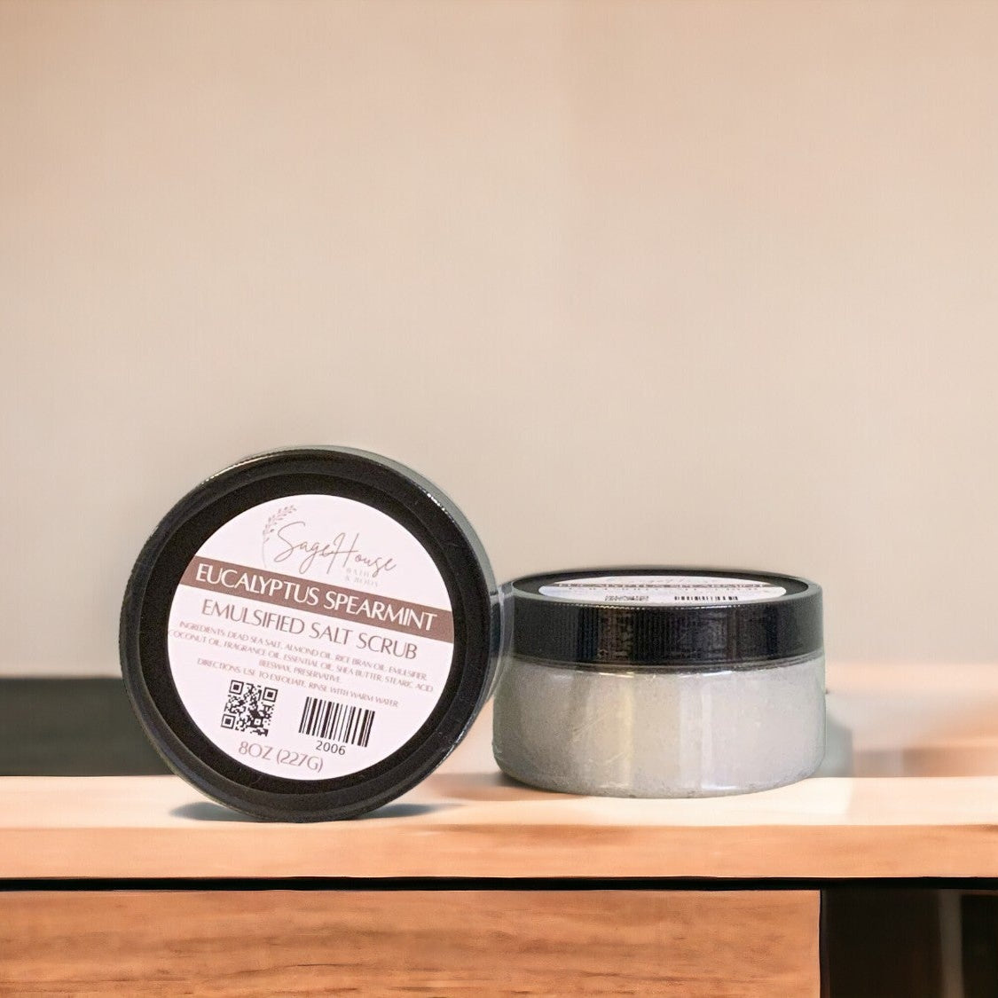 A jar of Eucalyptus Spearmint Salt Scrub with black lid. placed on a wooden surface.
