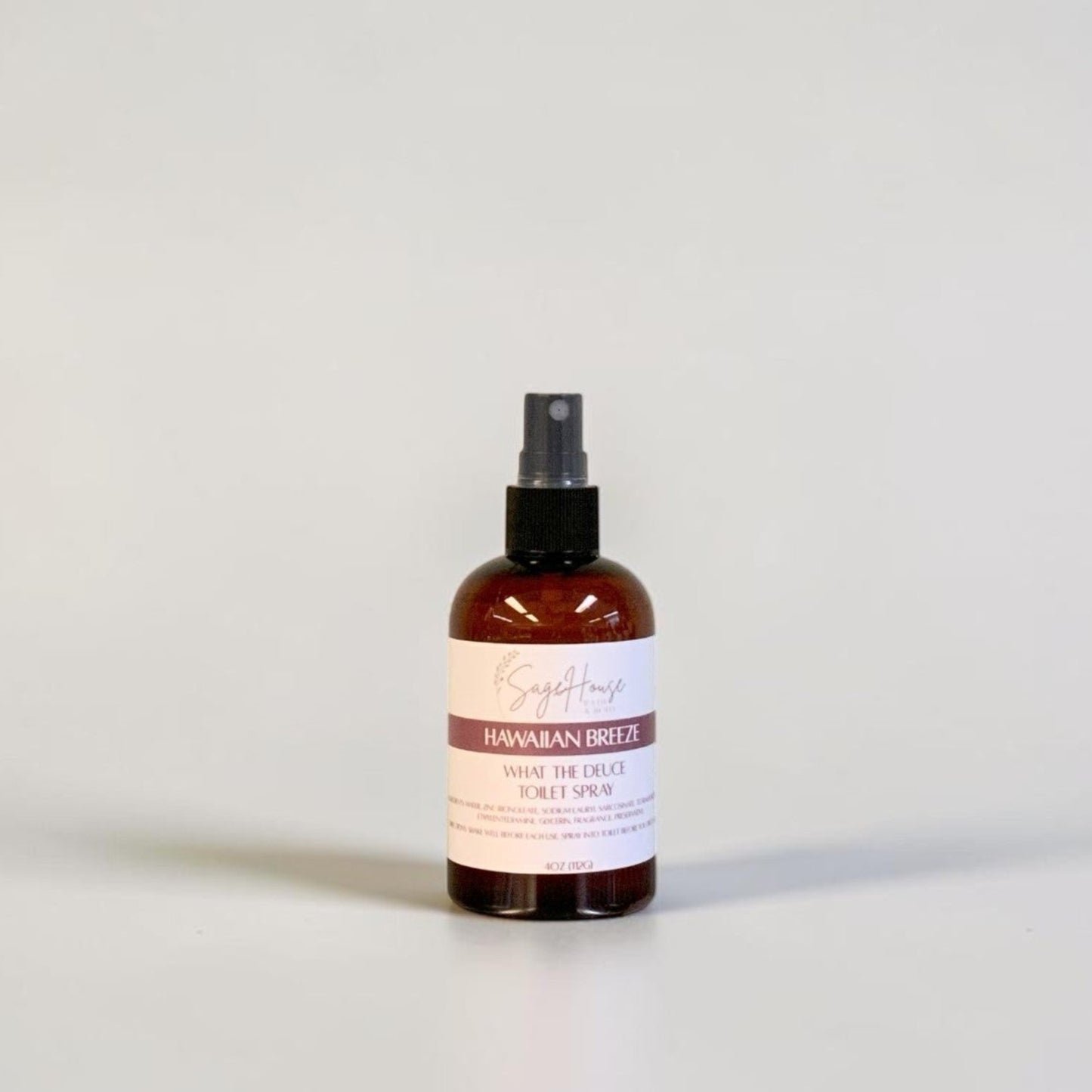 An amber spray bottle with black spray nozzle and white label, standing on a light gray surface against a light gray background.
