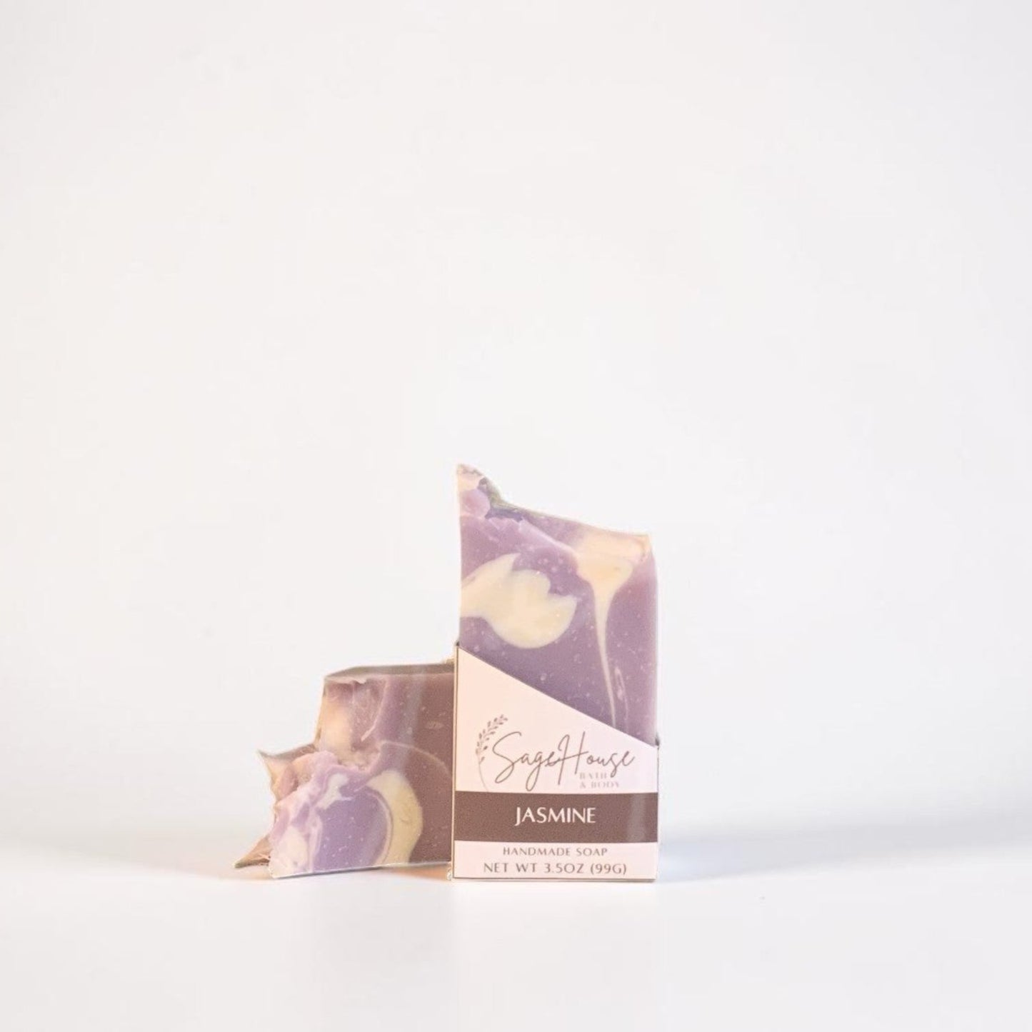 A small packaged soap bar with a purple and cream marbled pattern, standing upright next to a matching bar on a clean white background.