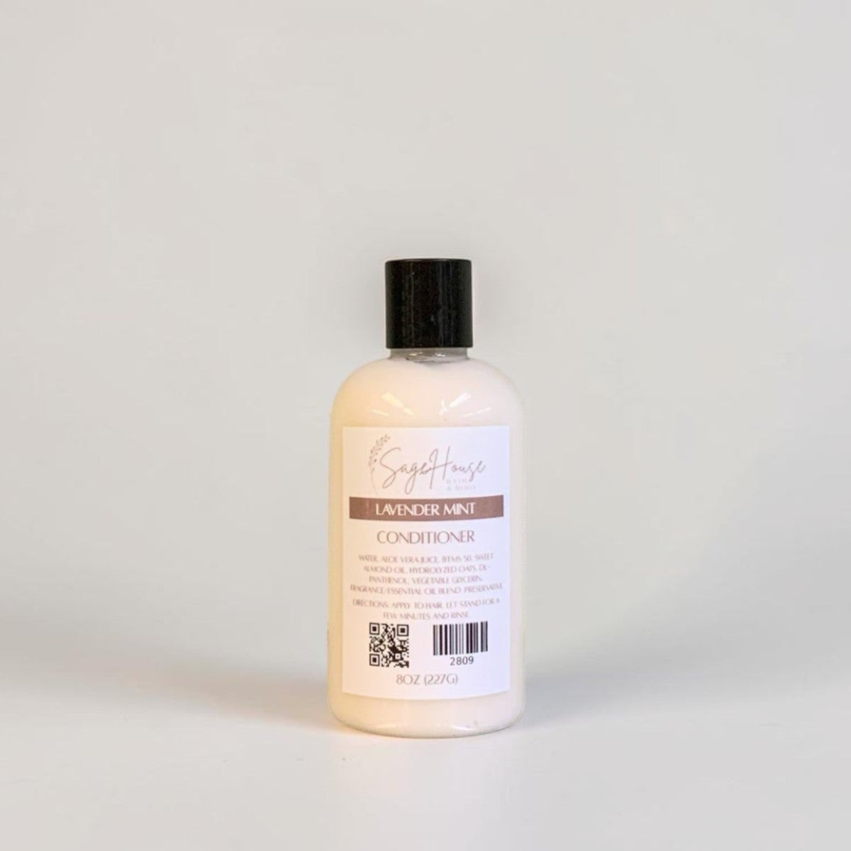 A bottle of conditioner with a black cap and white label. Sitting on a white background.