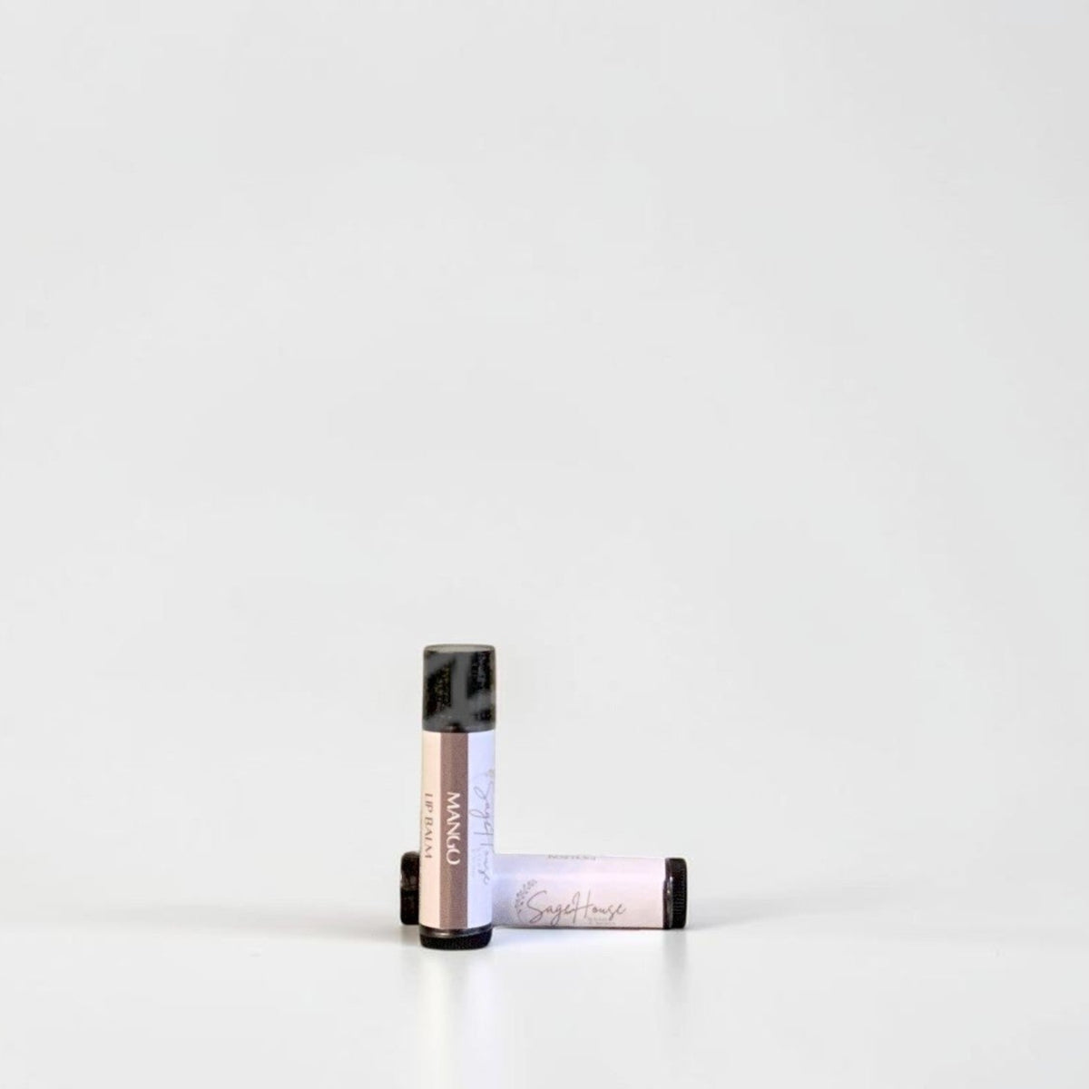 Two slim cylindrical lip balm tubes, one standing upright and one lying horizontally, positioned near the center of a clean white studio background.