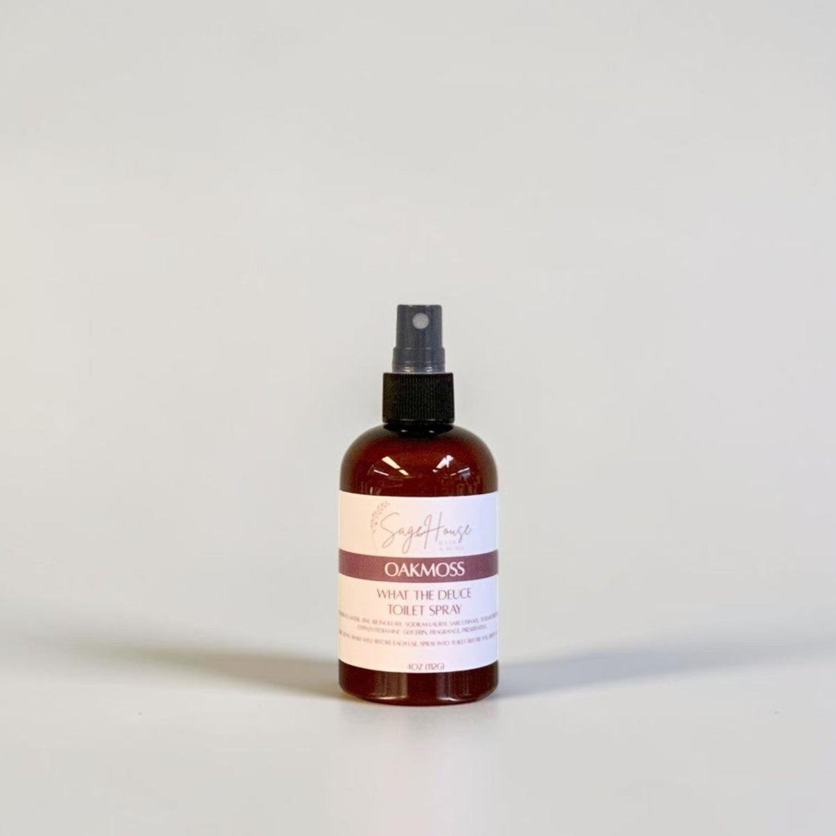 An amber spray bottle with black spray nozzle and white label, standing on a light gray surface against a light gray background.