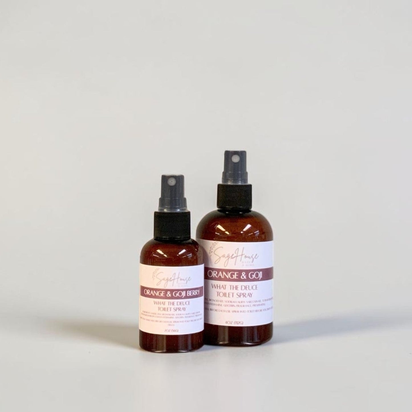 Two amber spray bottles with black spray nozzles and white labels, standing side by side on a light gray surface against a light gray background.
