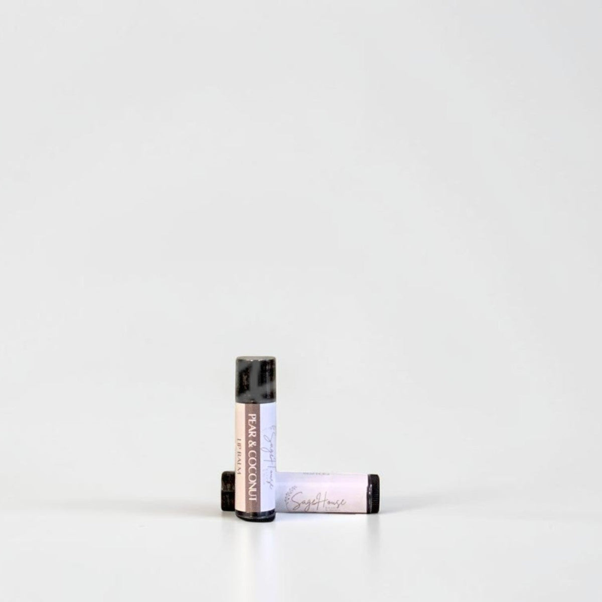 Two slim cylindrical lip balm tubes, one standing upright and one lying horizontally, positioned near the center of a clean white studio background.