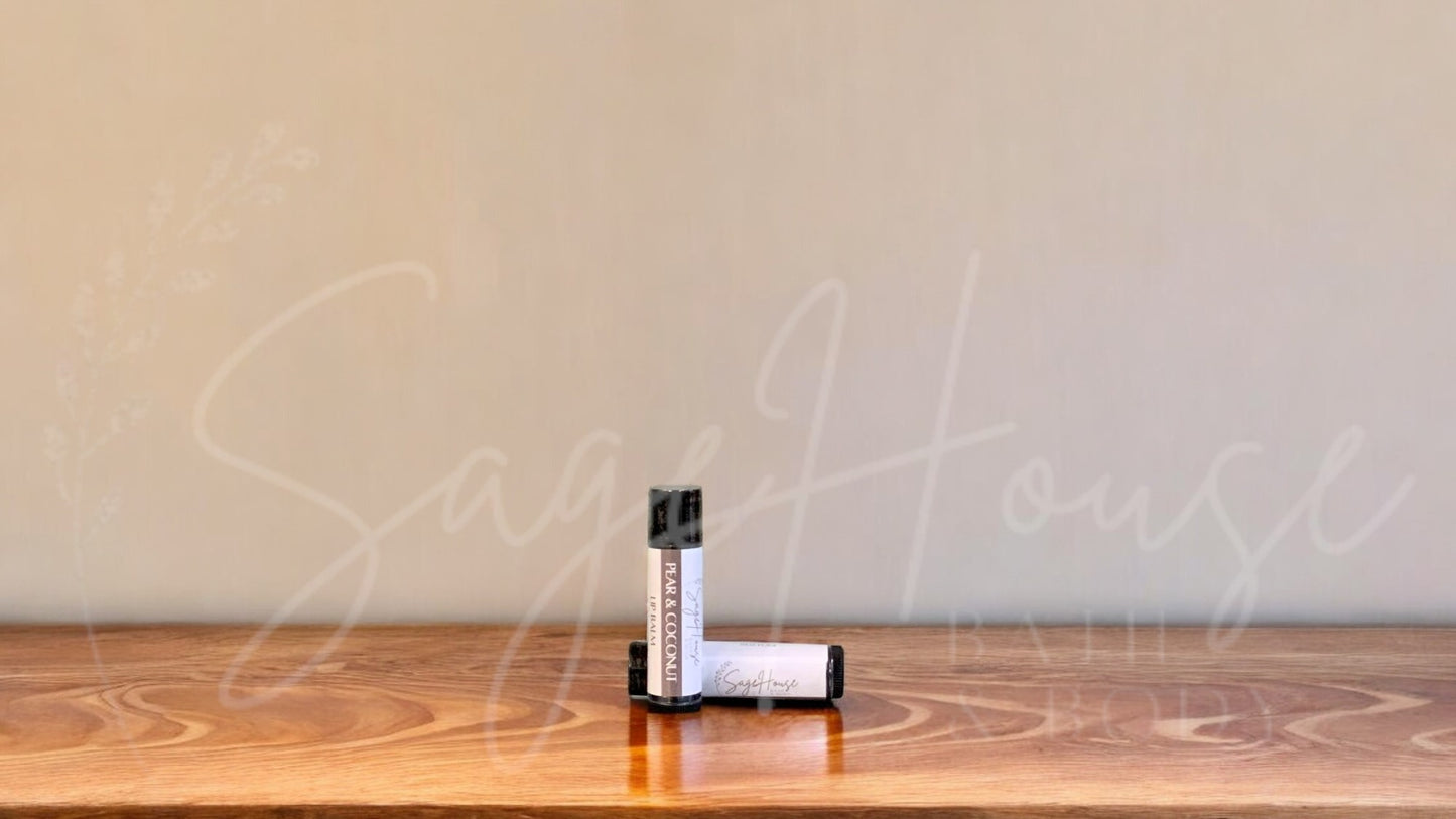 A tube of pear and coconut lip balm placed upright with a tube lying behind it, on a wooden surface.