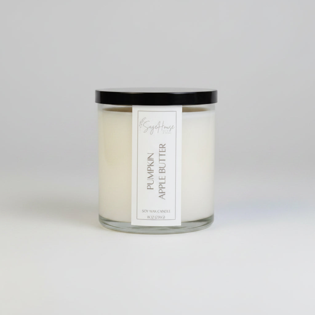 A white soy wax candle in a clear container, placed on a wooden surface, with a label on the front.