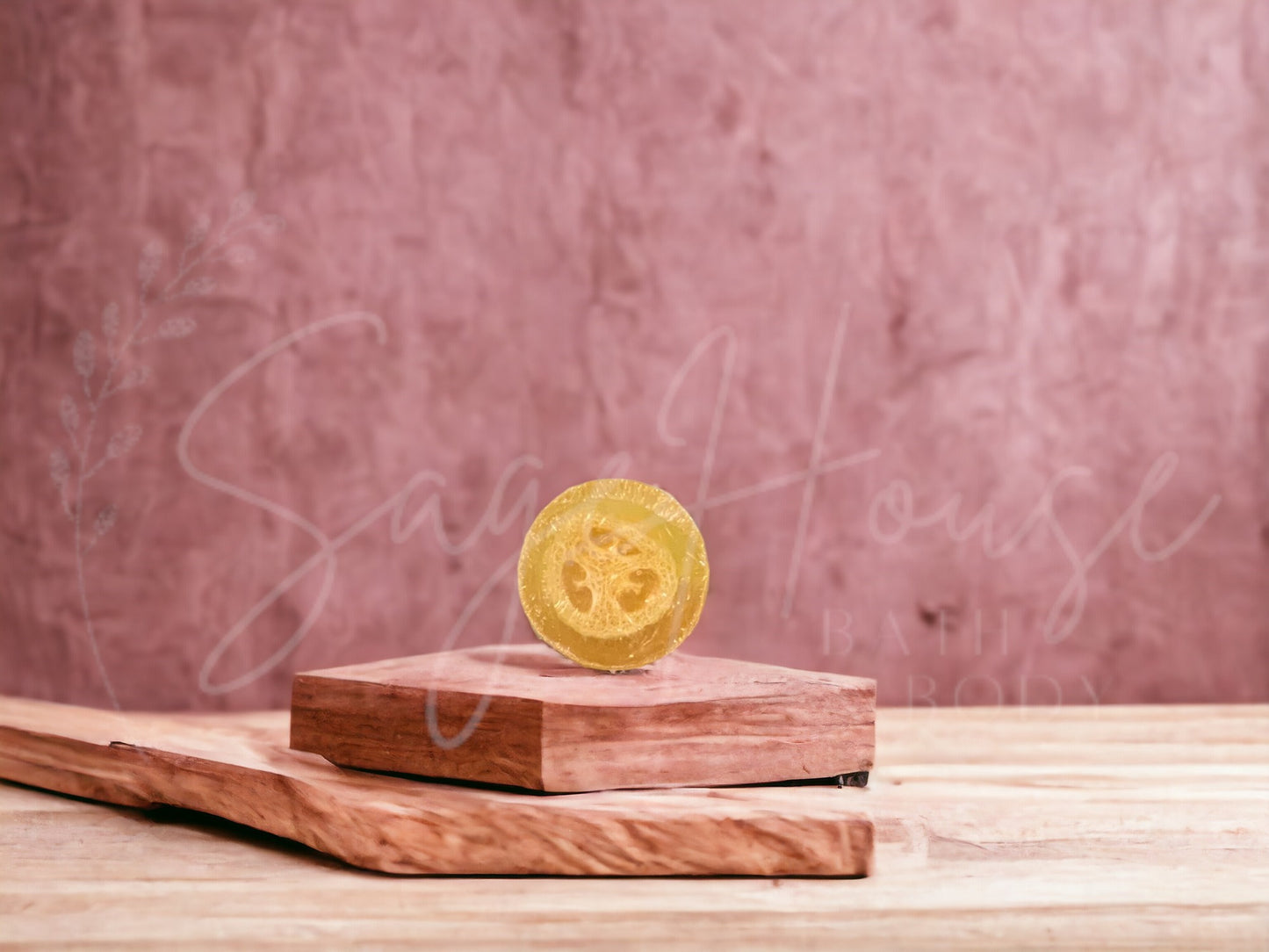 A yellow bar of raspberry lemonade loofah soap resting on a wooden soap dish, with a pink background.