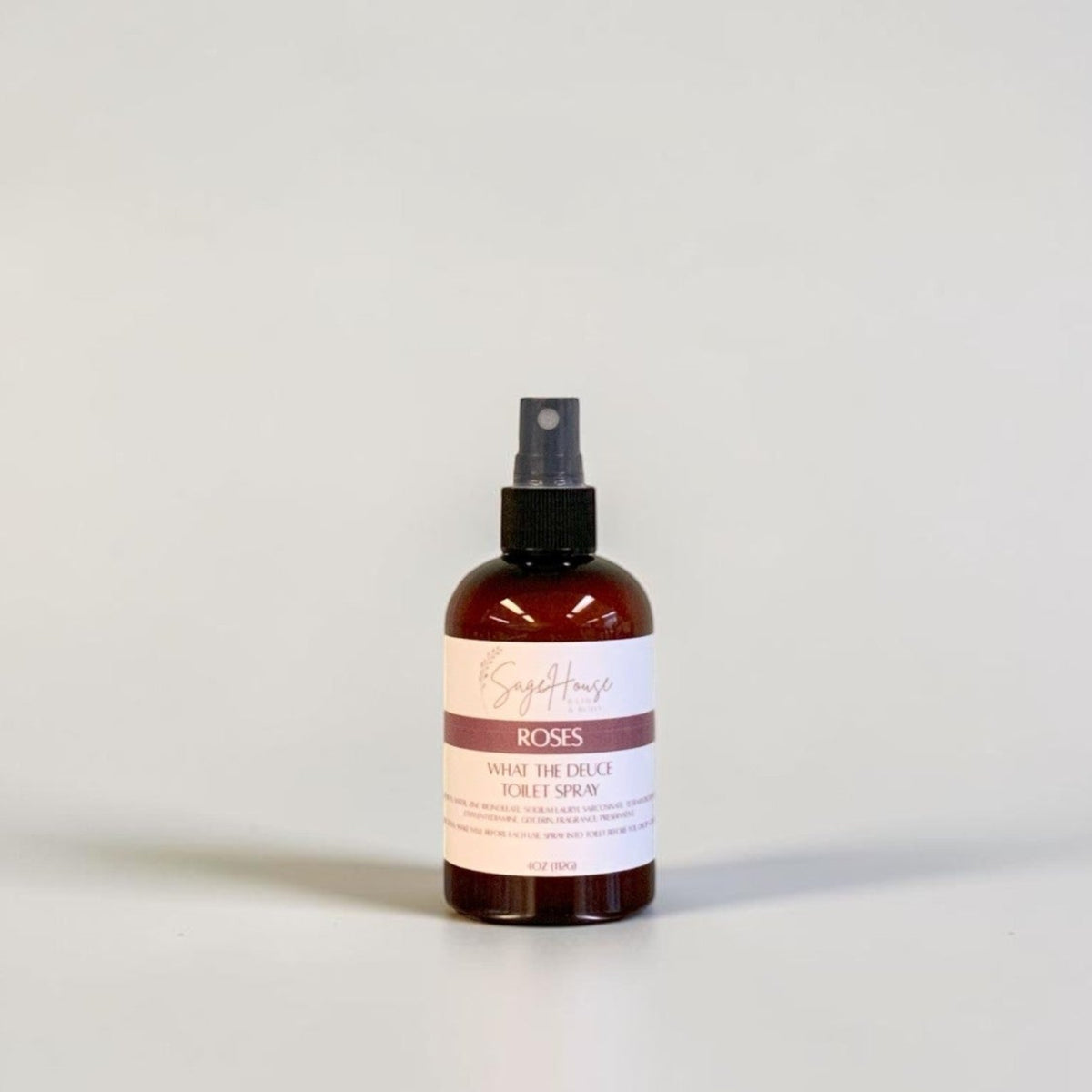 An amber spray bottle with black spray nozzle and white label, standing on a light gray surface against a light gray background.
