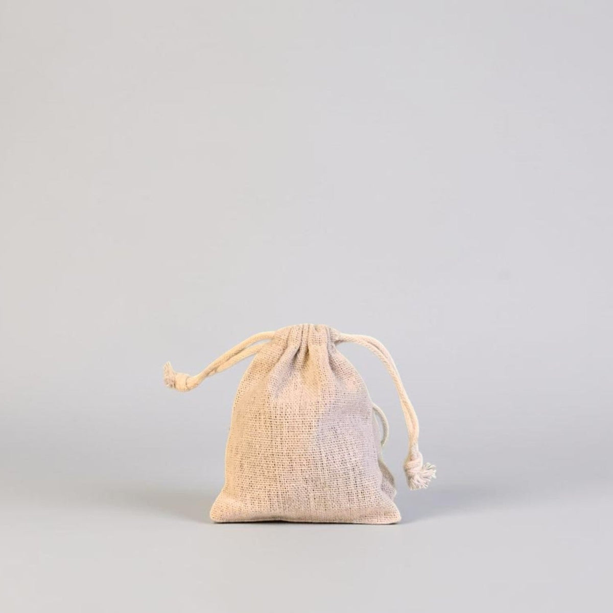 A small beige linen drawstring pouch standing upright on a light gray background.