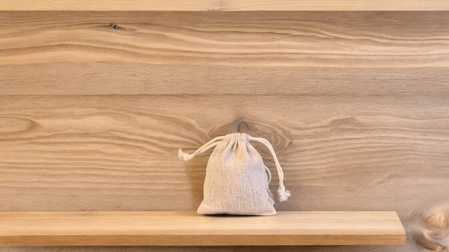 A beige-colored scented sachet with a drawstring closure, placed on a wooden surface.