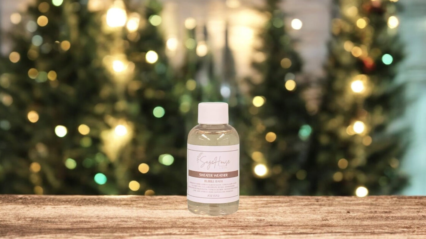 A small bottle of bubble bath, with white lid. On a wood top with greenery in the background.