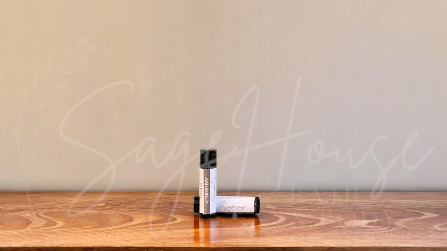 A tube of watermelon lip balm placed upright with a tube lying behind it, on a wooden surface.
