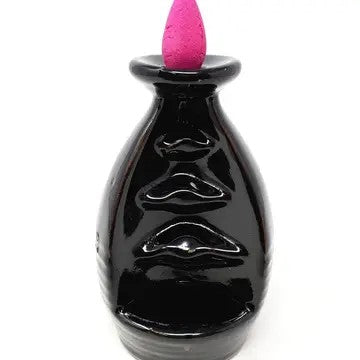 A small black waterfall cone incense burner with an incense cone placed on top