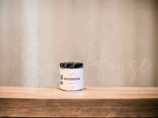 A container of Almond & Honey Body Butter placed on a wooden surface with a textured background.