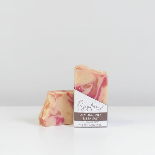 A white bar of soap w/ pink & gold accents in a white labeled open box. on a wood surface.