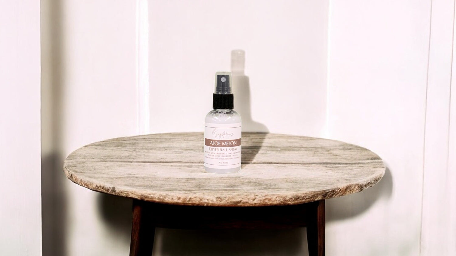 A clear bottle with black spritz top. sitting on a stone table with a white wall in the background