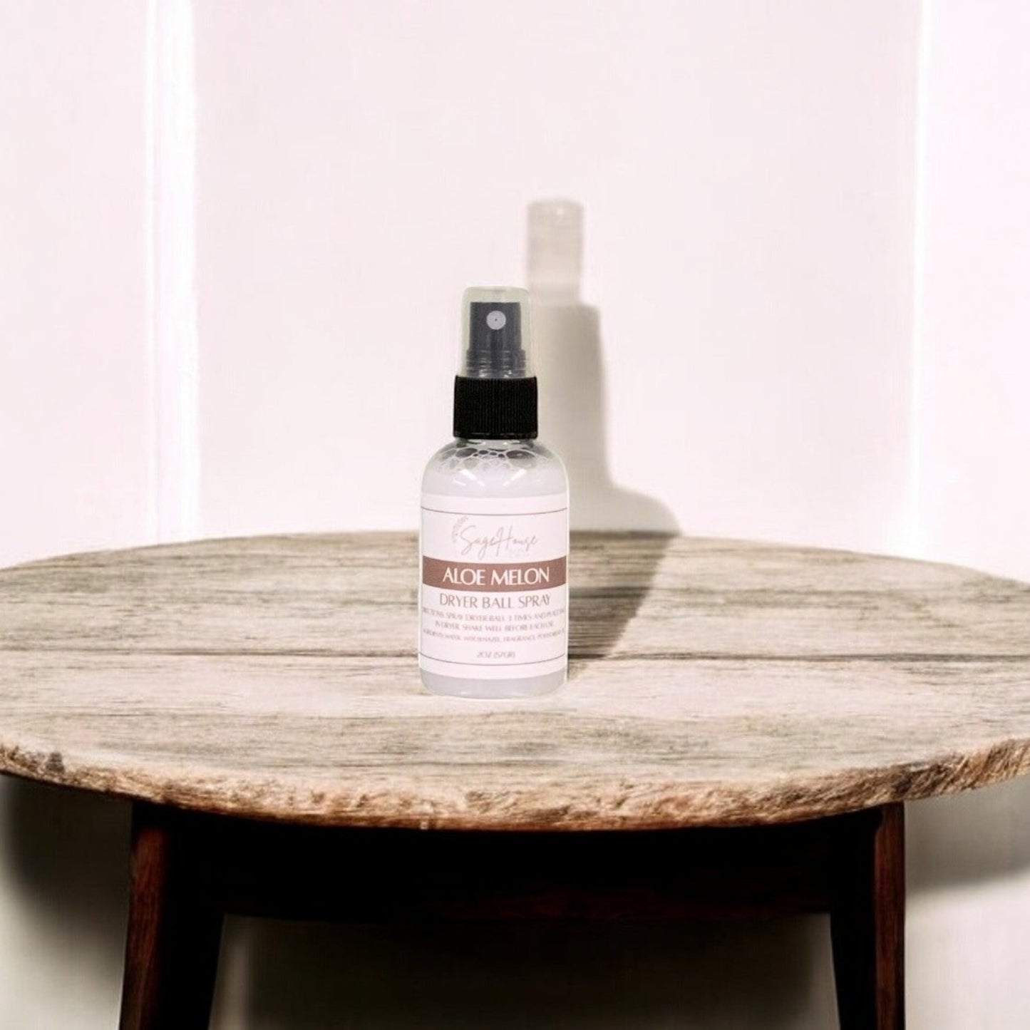 A clear bottle with black spritz top. sitting on a stone table with a white wall in the background