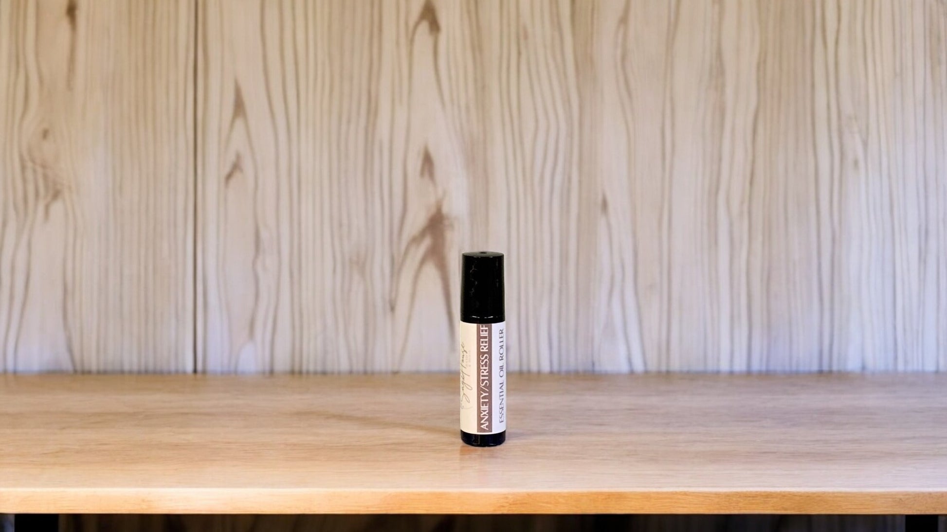 A roller bottle, labeled with 'Anxiety/Stress Relief Massage Oil', positioned on a wooden surface.