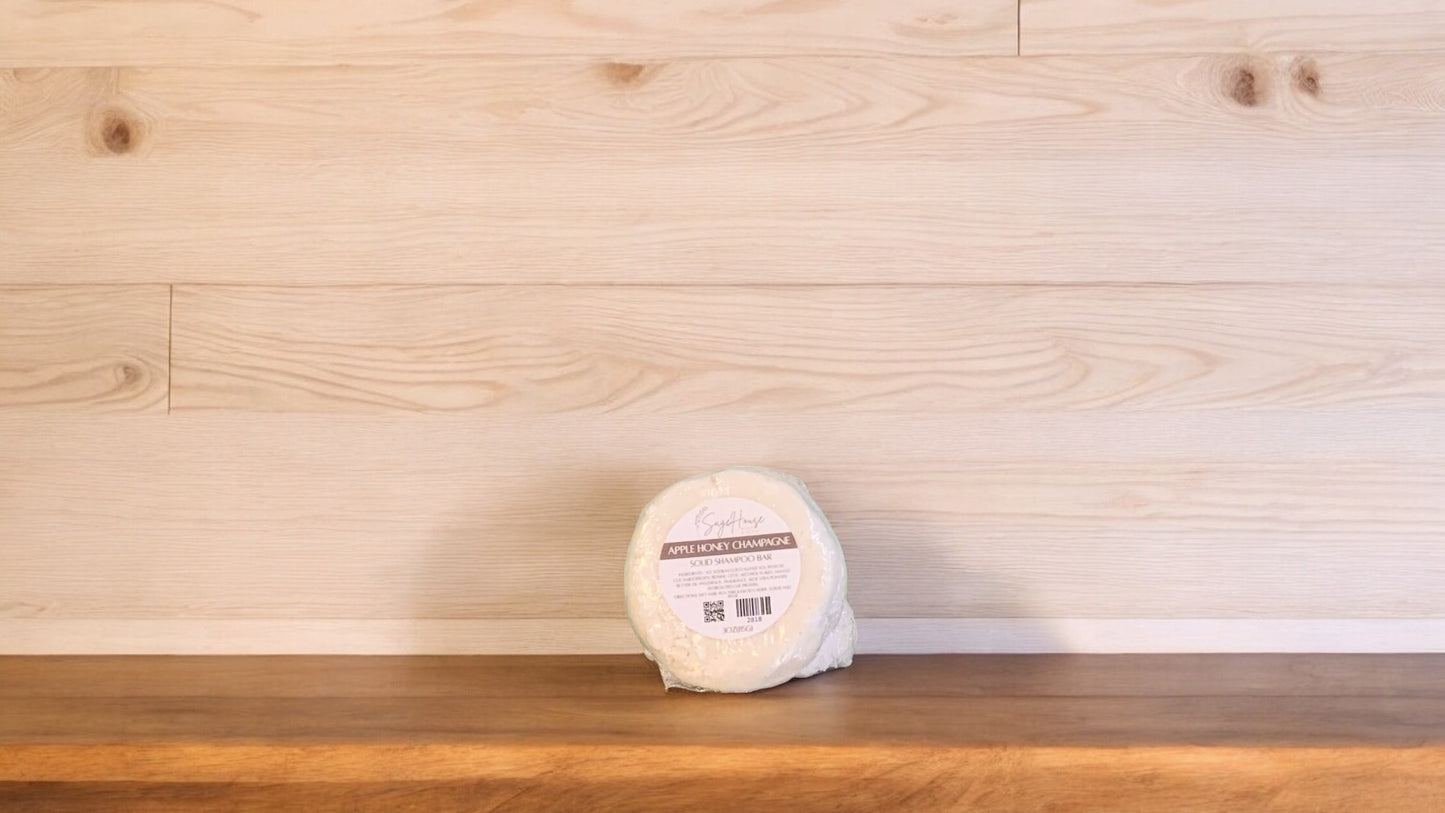 An Apple Honey Champagne shampoo bar sitting on a wood surface with light wood in the background