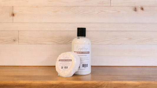An Apple Honey Champagne shampoo bar and bottle of conditioner on a wooden surface.