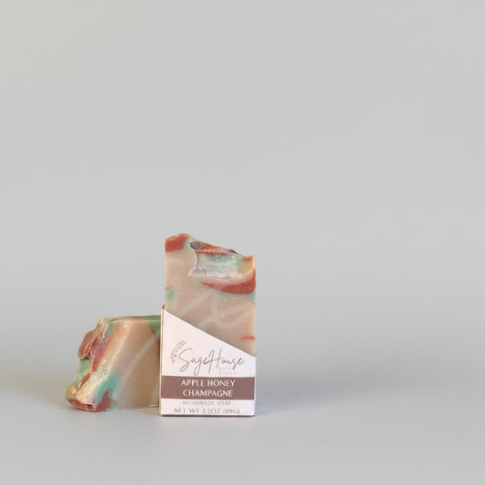 A tan bar of soap w/ red accents in a white labeled open box. on a wood surface.