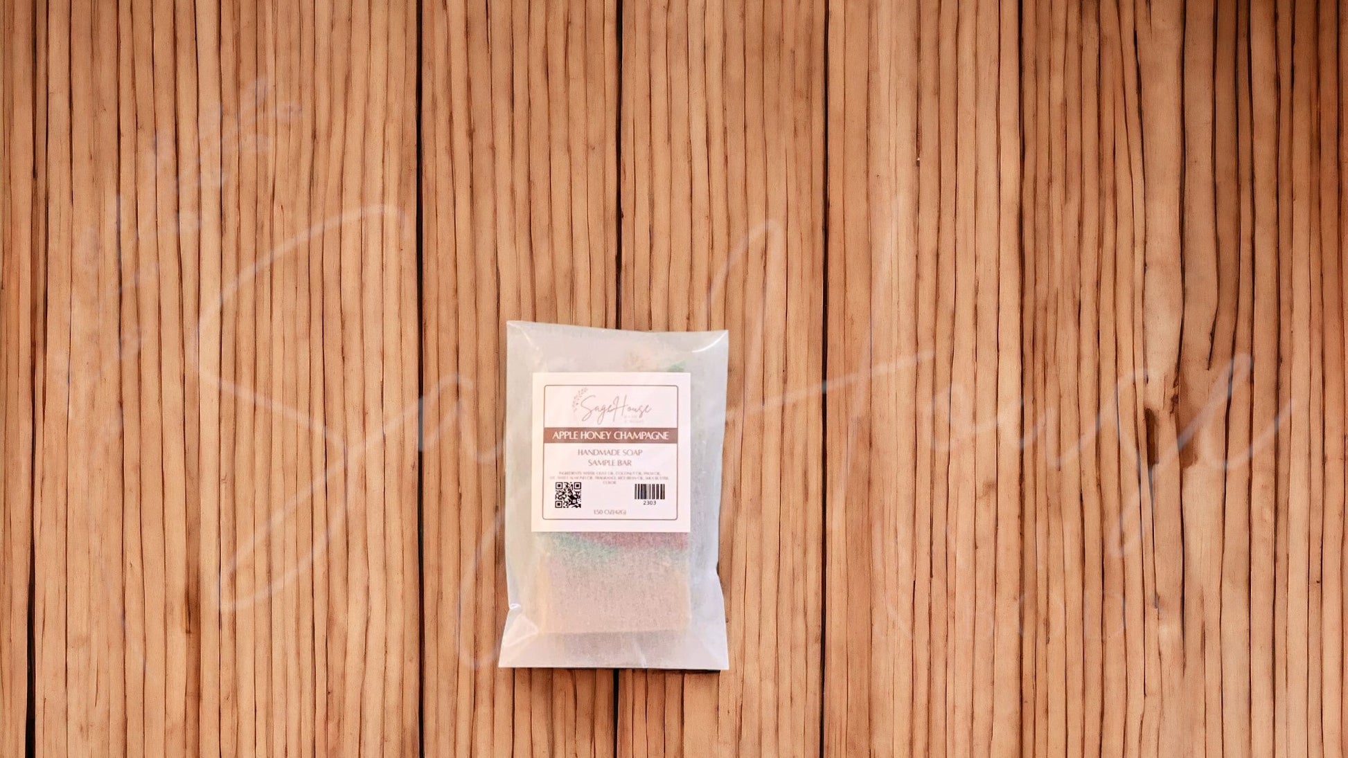 A sample bar of soap in a frosted glassine bag with a label. on a wood surface.
