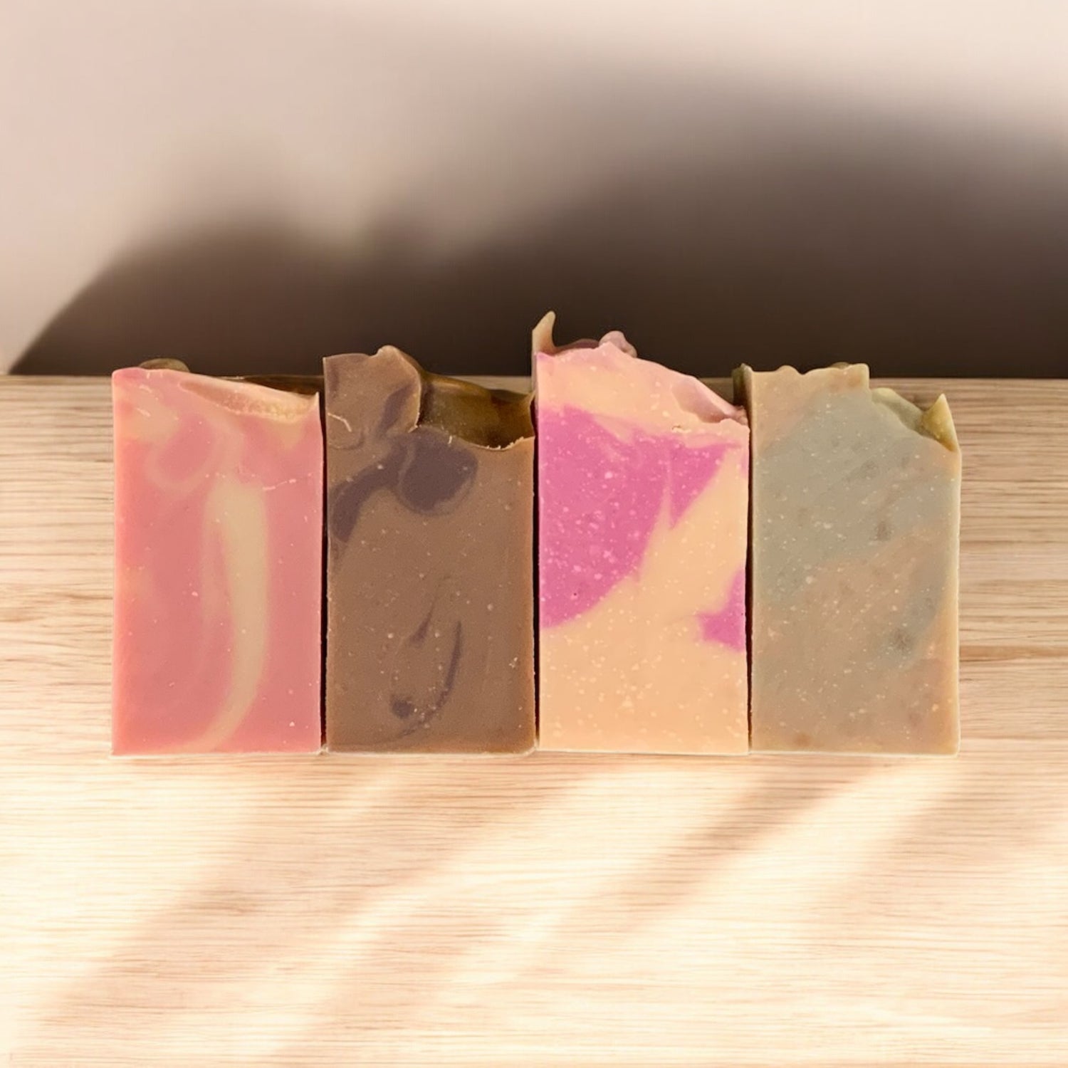 Four different colored soap bars on a wooden surface