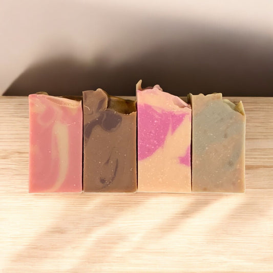 Four different colored soap bars on a wooden surface