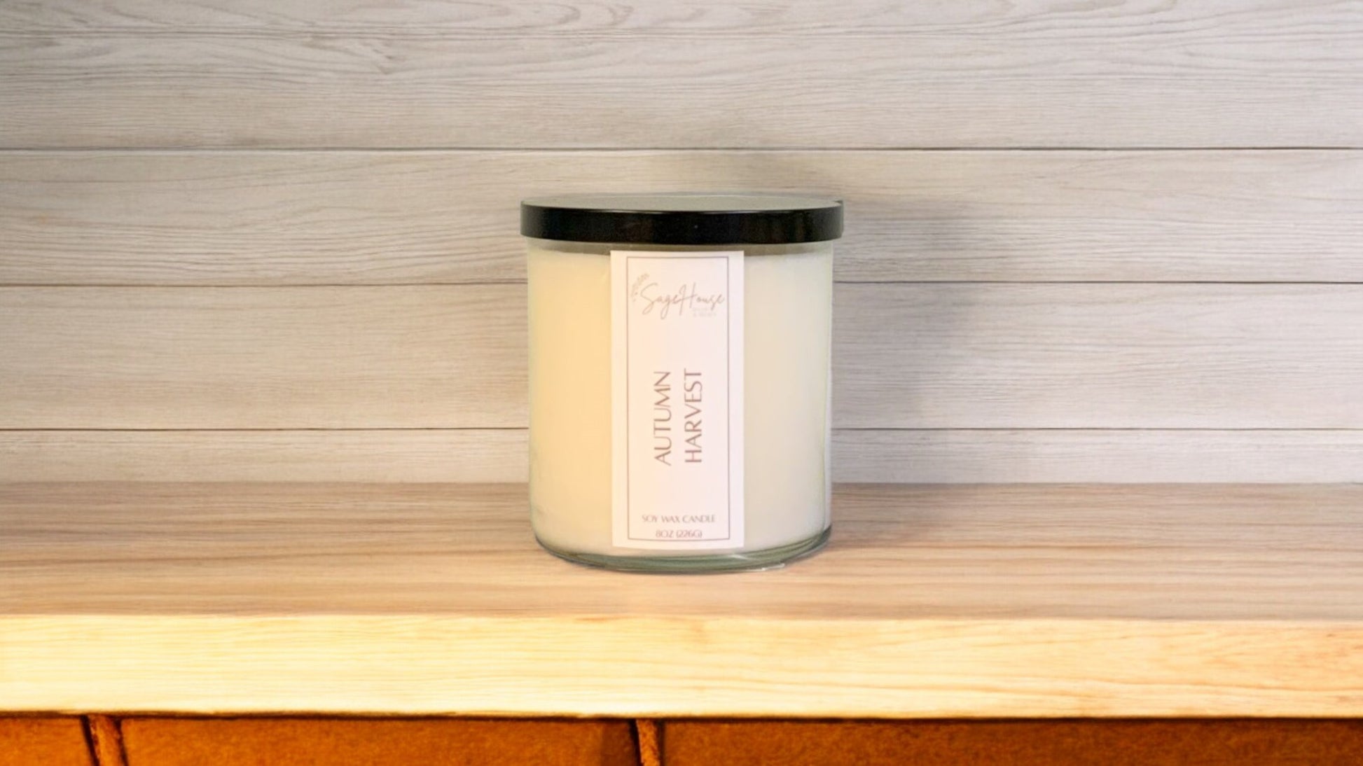 A white soy wax candle in a clear container, placed on a wooden surface, with a label on the front.