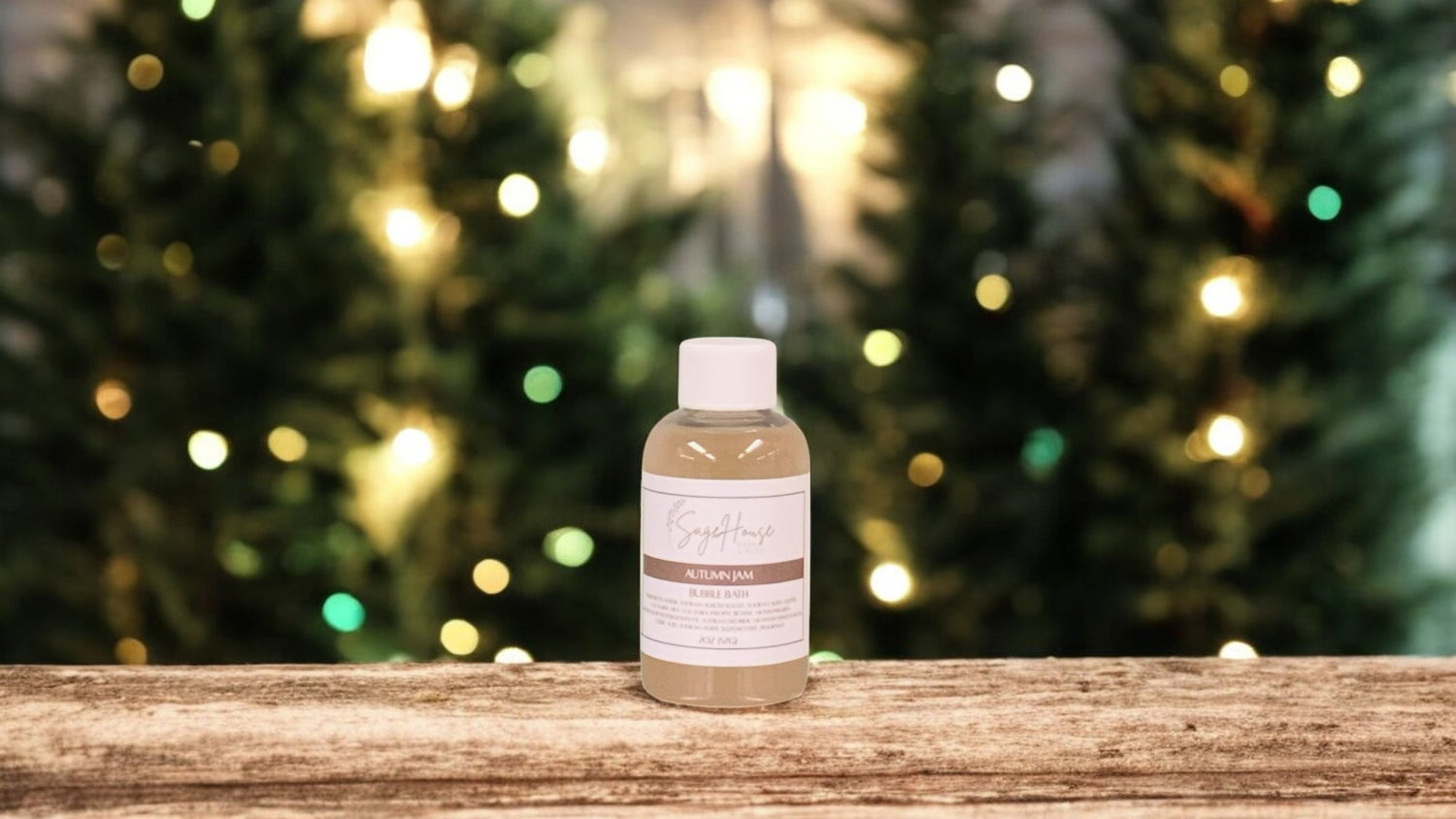 A small bottle of bubble bath, with white lid. On a wood top with greenery in the background.