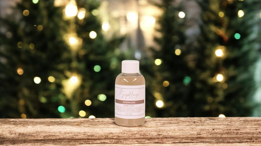 A small bottle of bubble bath, with white lid. On a wood top with greenery in the background.