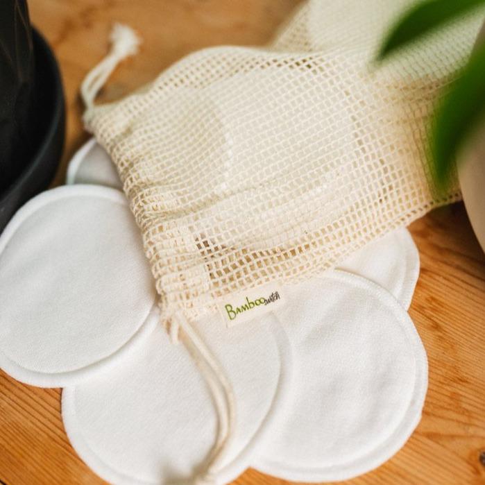 bamboo facial rounds laid out on a wooden surface with a single organic cotton washable mesh bag on top.