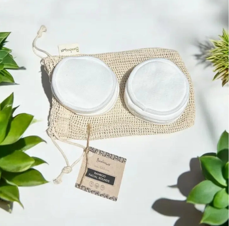 Two stacks of bamboo facial rounds on a mesh bag, on a white surface. with a plant in the background