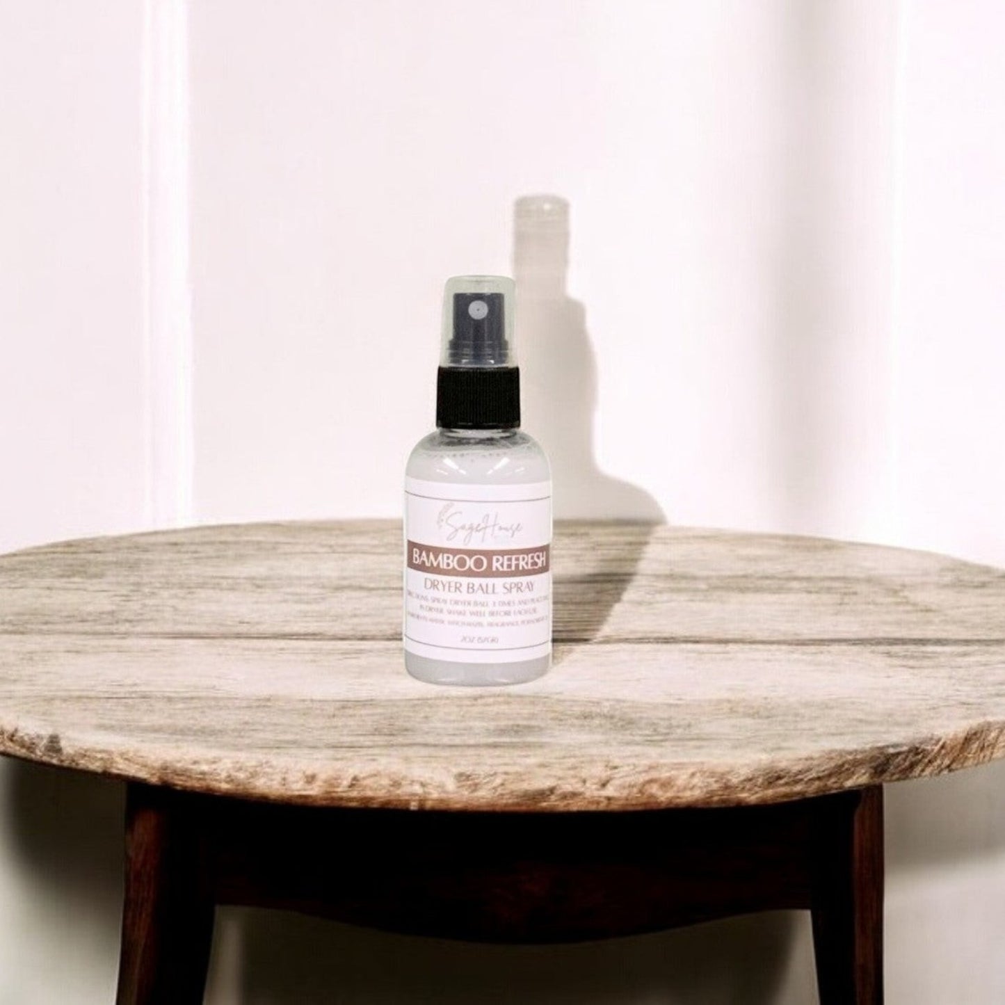 A clear bottle with black spritz top. sitting on a stone table with a white wall in the background