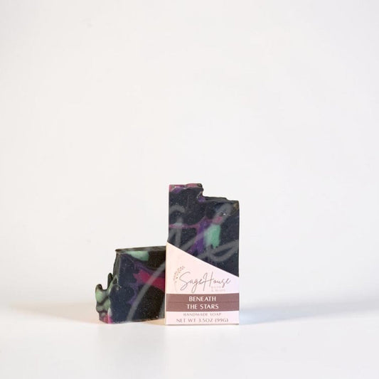 A dark bar of soap with a label, standing on a white surface against a white background.