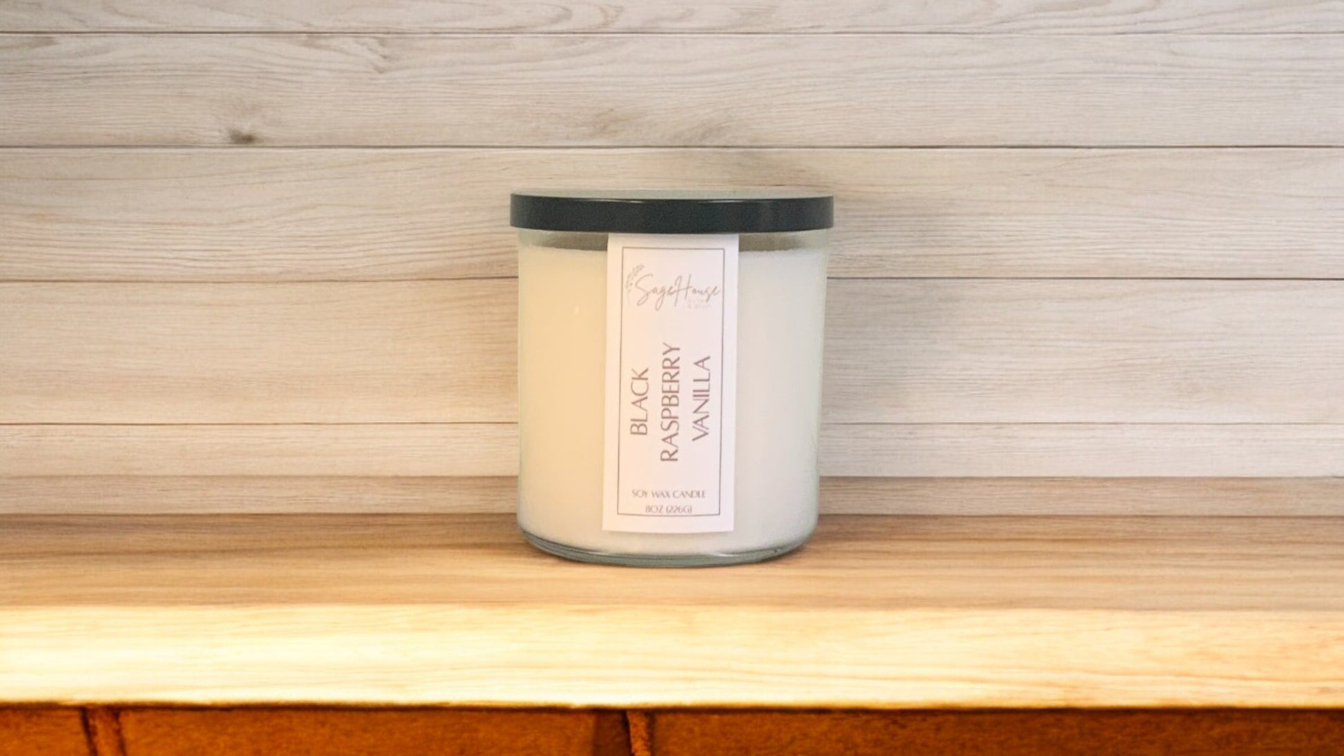 A white soy wax candle in a clear container, placed on a wooden surface, with a label on the front.