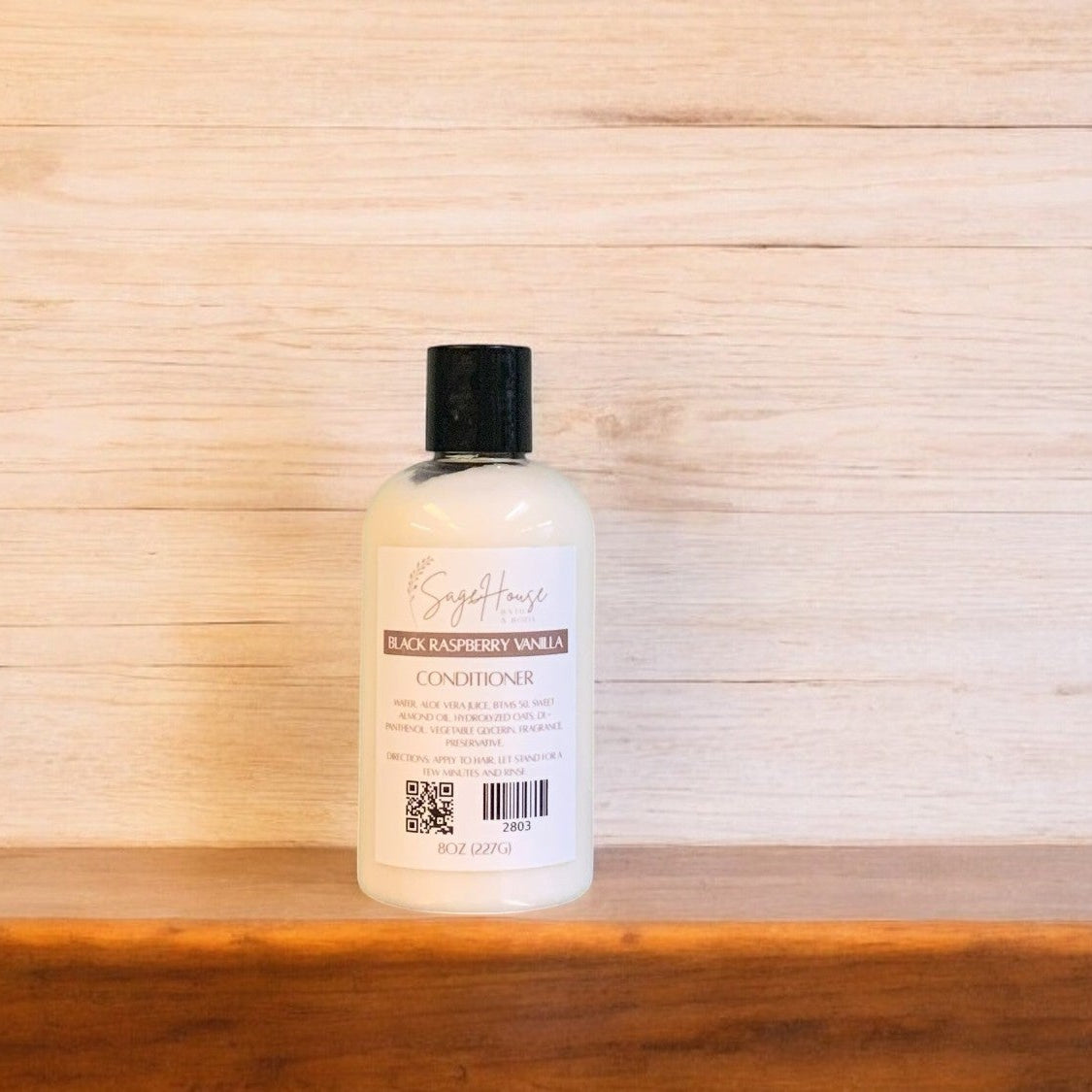 A Sage House Black Raspberry Vanilla conditioner in a clear bottle on a wooden surface.