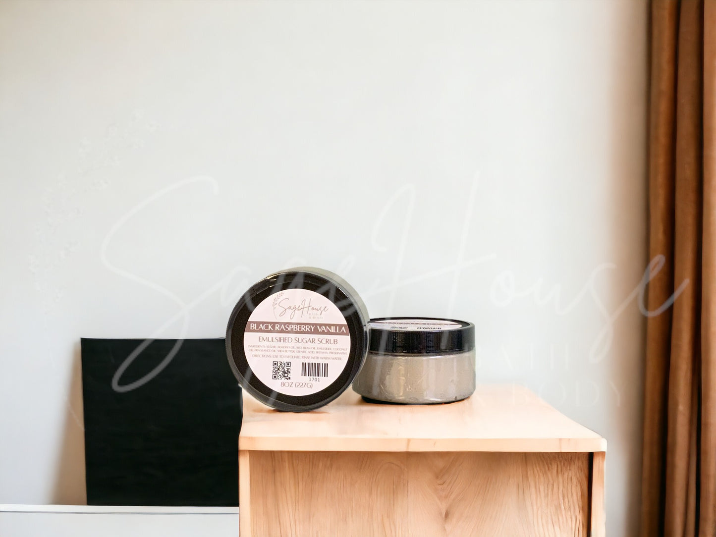 Two jars of scrub, one standing next to the other, sitting on a wooden surface with a white background