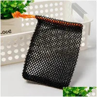 A Soap Scrub Pouch in black, placed on a white surface. A basket and plant in the background.